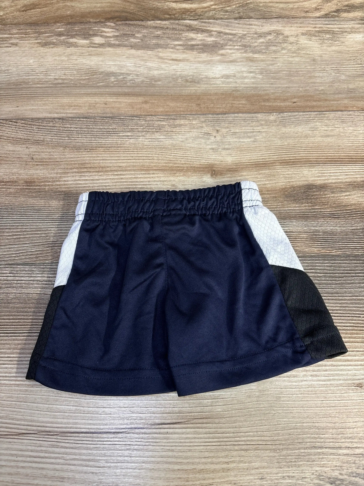 Front view of navy NBA pull-on baby shorts 3-6mo with elastic waistband and white/black side panels on wood