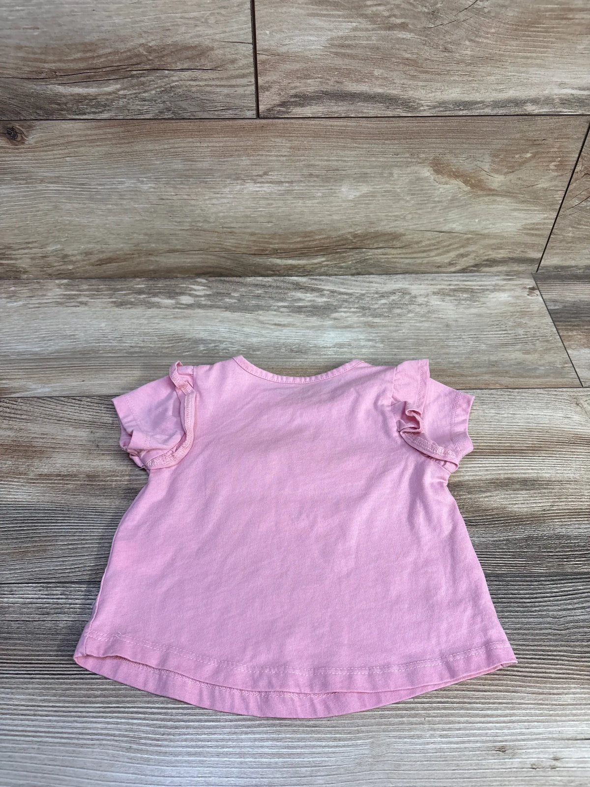 Front view of pink Lucky Penny bear shirt, size 2T, showcasing flutter sleeves and a curved hem on a wood-look floor