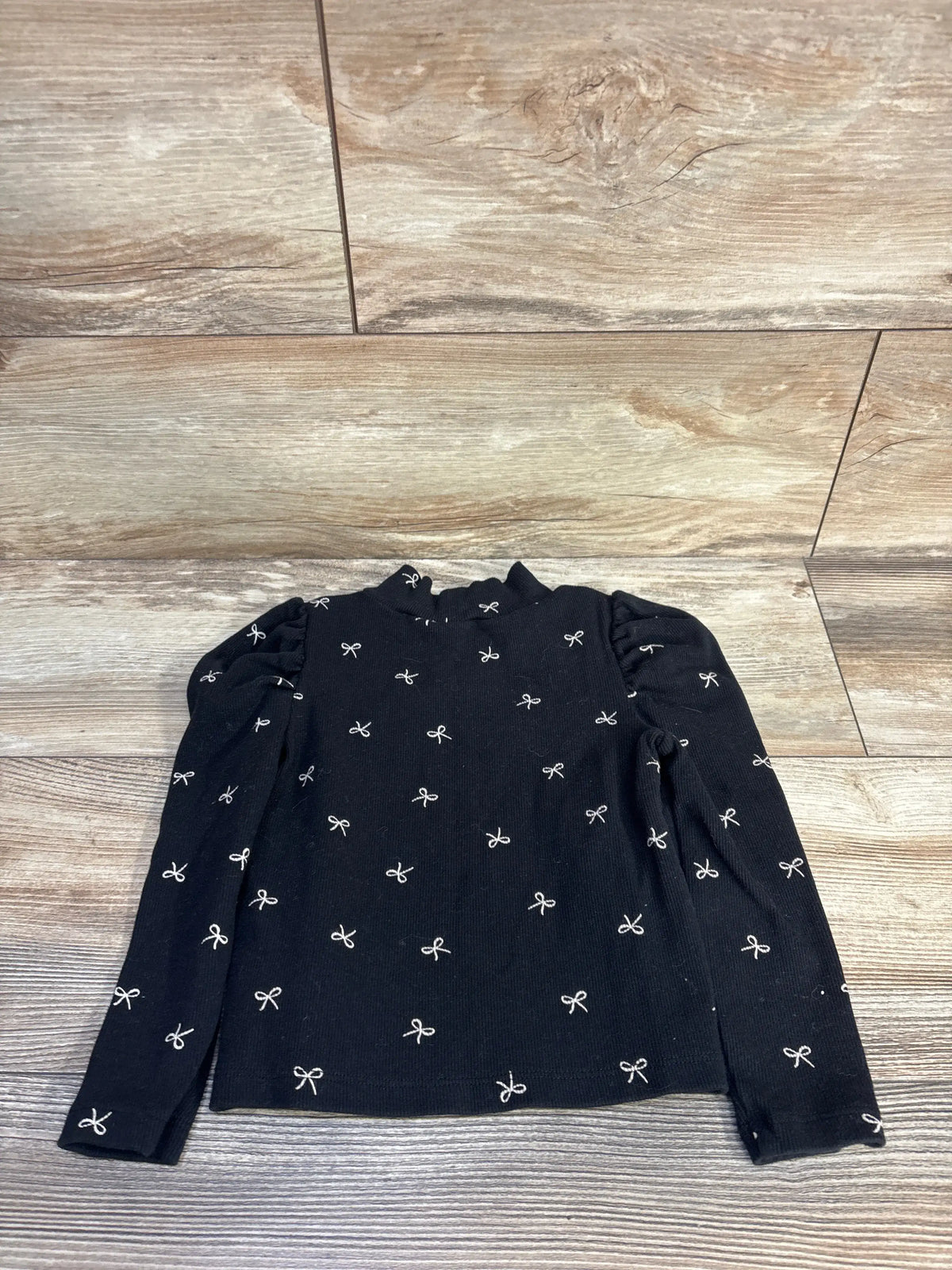 Flat lay of Baby Gap black ribbed mockneck long sleeve shirt in size 3T showcasing puff sleeves and allover bow print