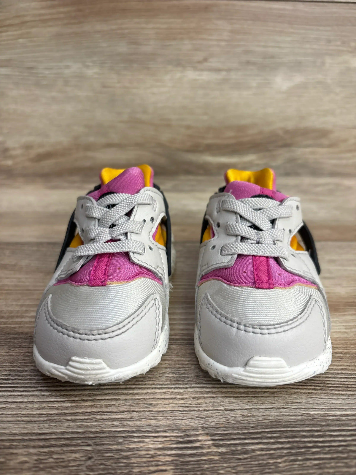 Pair of toddler sneakers with gray, pink, yellow, and black accents on wood floor