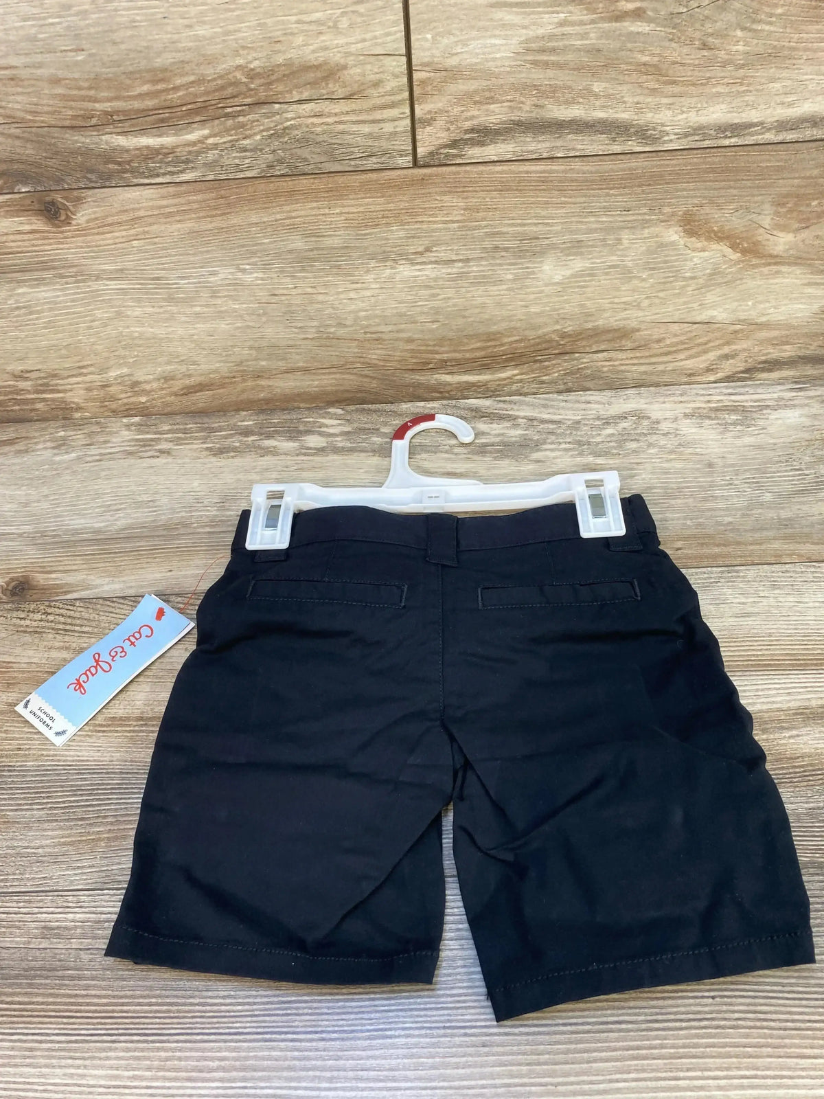 Back view of Cat & Jack toddler black school uniform shorts showing faux back welt pockets and belt loop on wood floor background