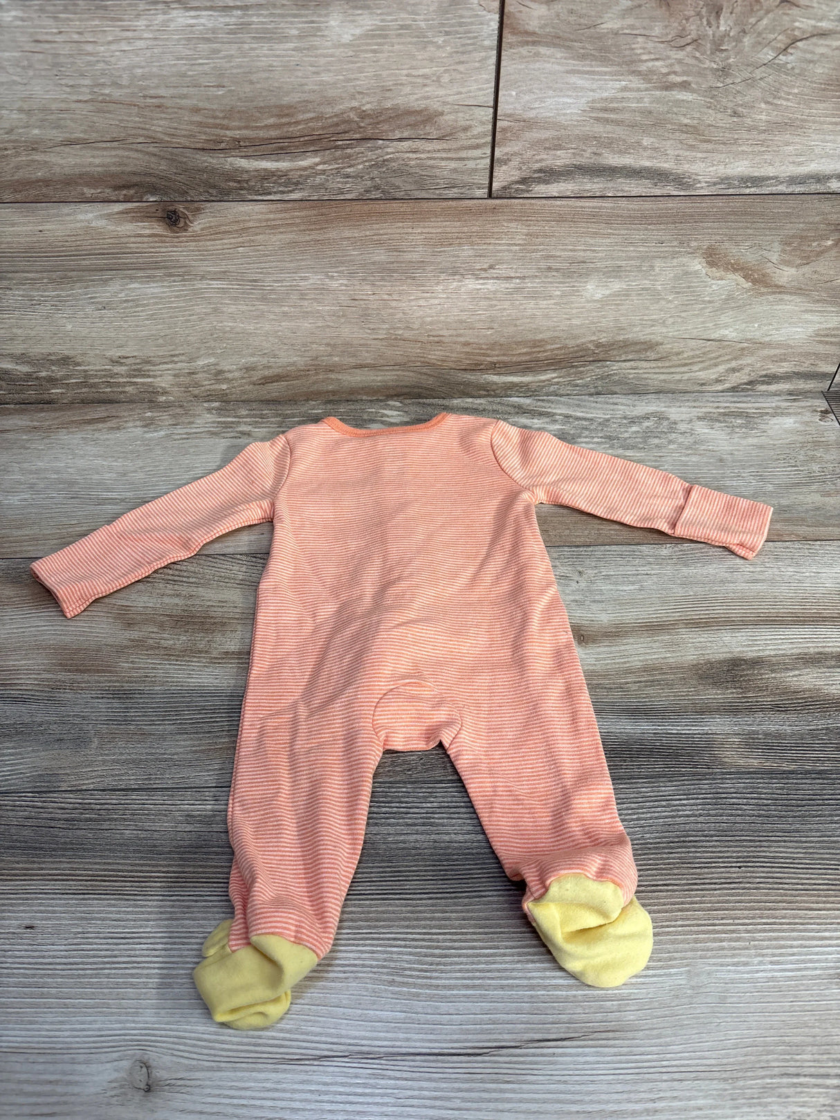 Pink striped baby footed pajamas with yellow cuffs on wood floor