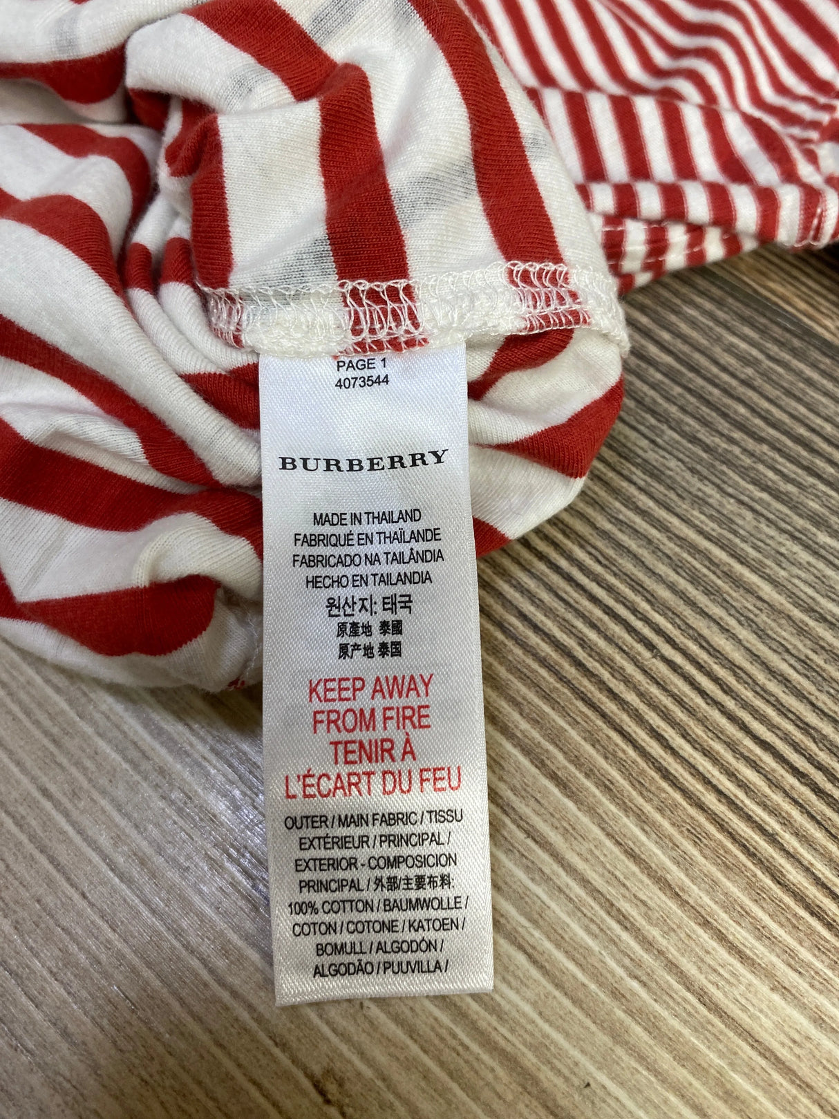 Burberry clothing label on red and white striped fabric showing manufacturing details and fire safety warning