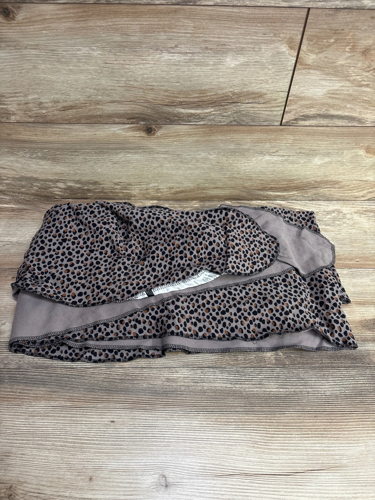Top-down view of Moby Classic Wrap baby carrier, cheetah print, folded to show soft jersey fabric and leopard-spot pattern on wooden floor