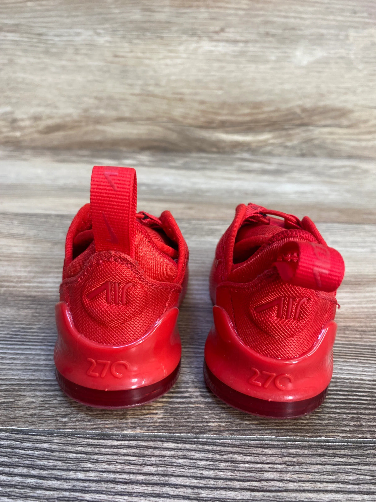 Pair of red kids' Nike Air 270 sneakers on wood floor, back view