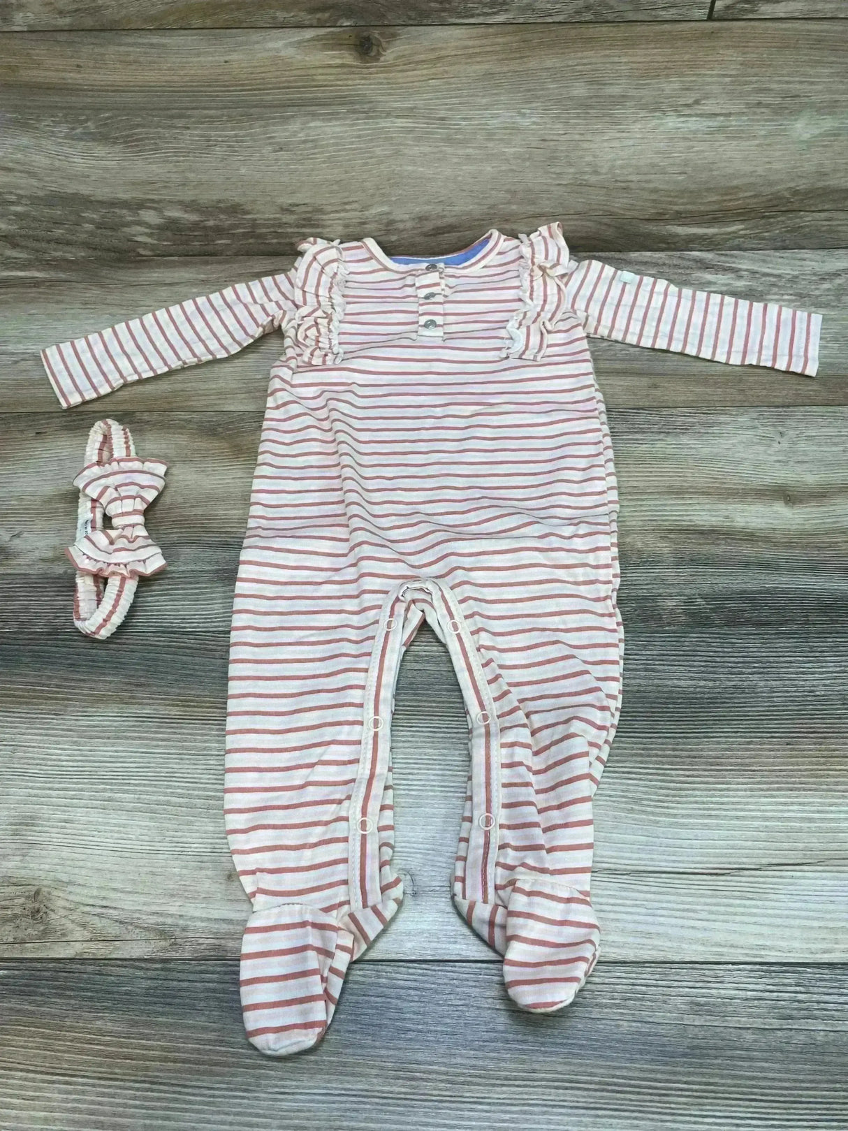 Flat lay of pink striped footed ruffle coverall, size 6-9M, with snap leg closures and matching headband on wood background