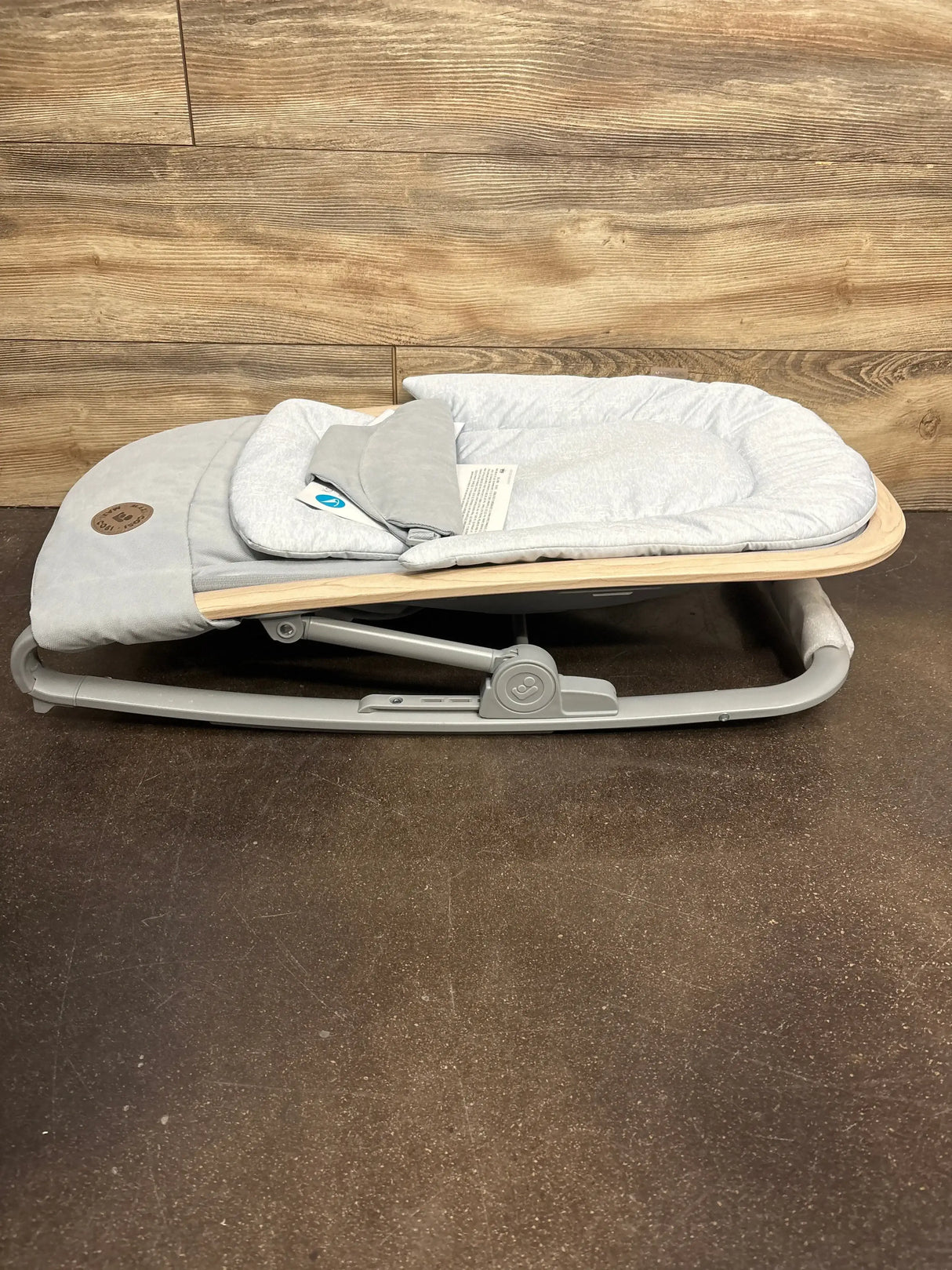 Side view of Maxi-Cosi Kori 2-in-1 baby rocker in classic slate showcasing padded infant seat and wood-accent frame against wood-paneled wall and brown floor