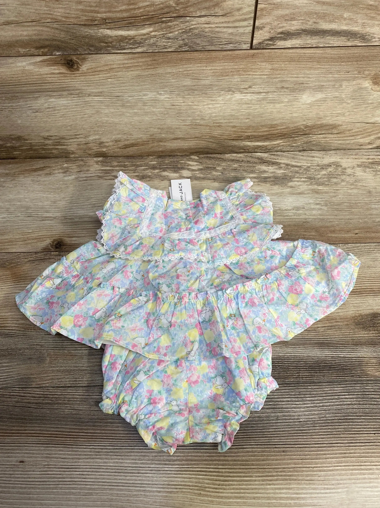 Flat lay of Janie and Jack 2-piece floral bunnies top and matching bloomers showcasing ruffled collar and lace trim on wooden background