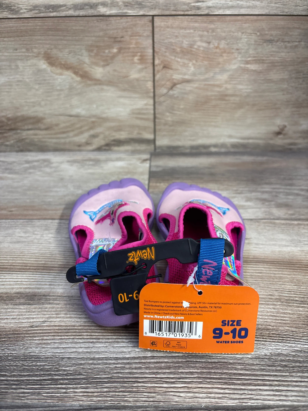 Front view of Newtz mermaid water shoes in pink and purple showing mermaid graphic, strap and size 9-10 tag on wood