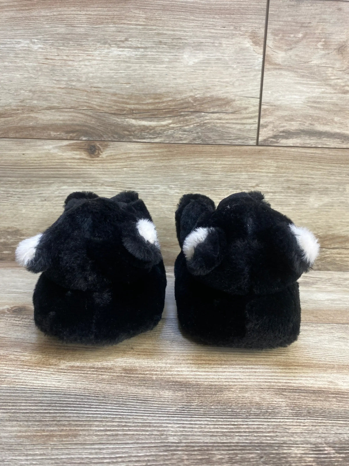 Rear view of Gap Cozy Bear baby slippers size 10-11C showing black plush bear design with white ear accents on wood background