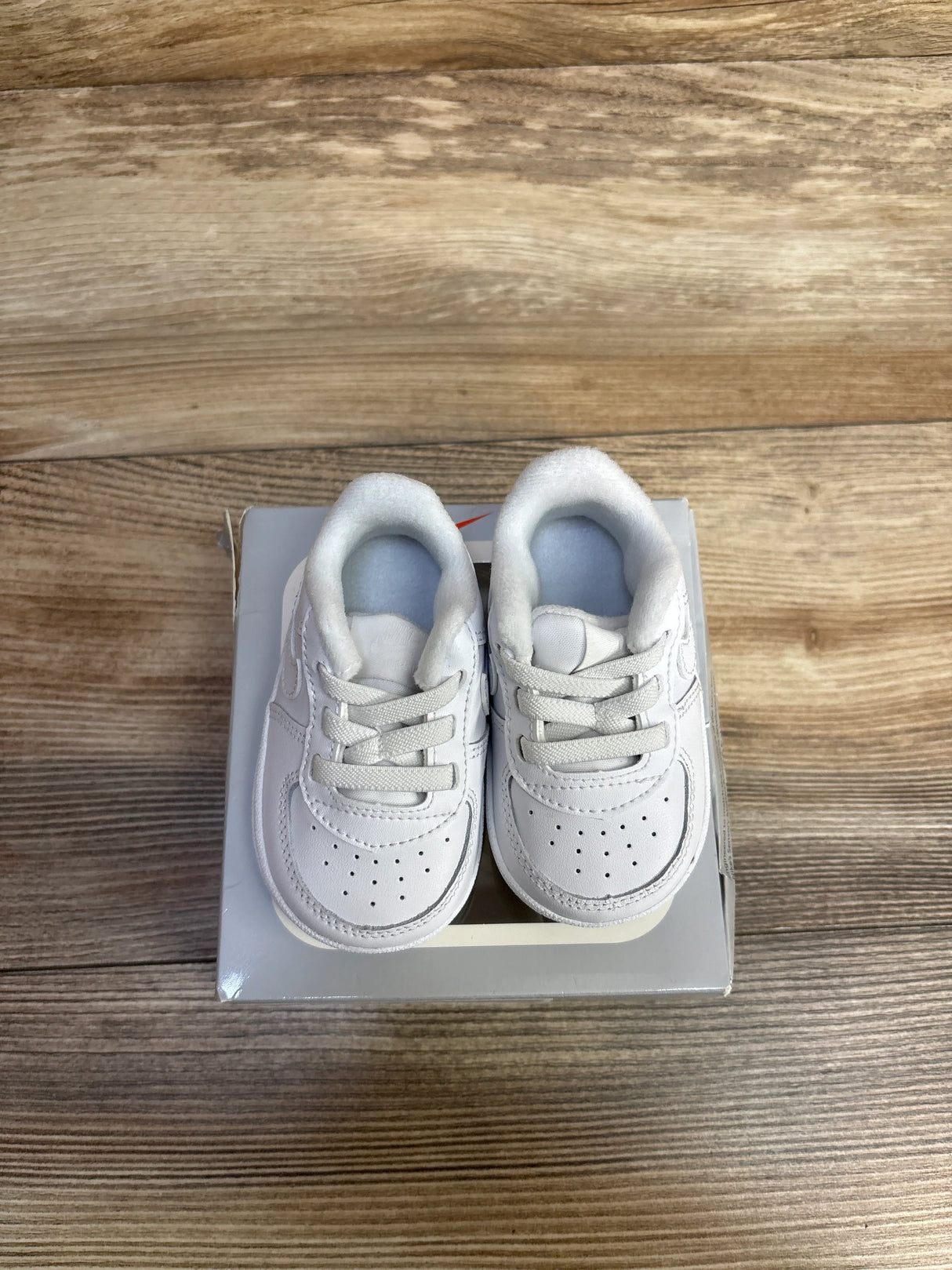 Pair of white baby sneakers placed on a gray shoebox on wooden floor