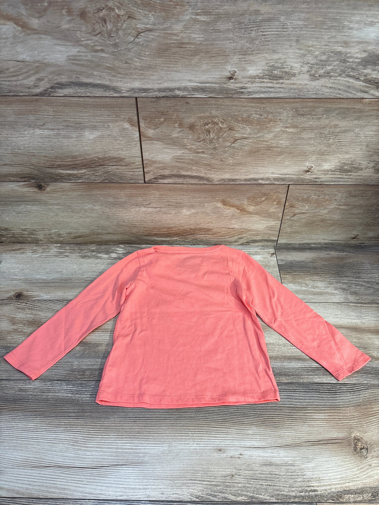 Back view of coral long-sleeve toddler shirt size 4T laid flat on wood floor