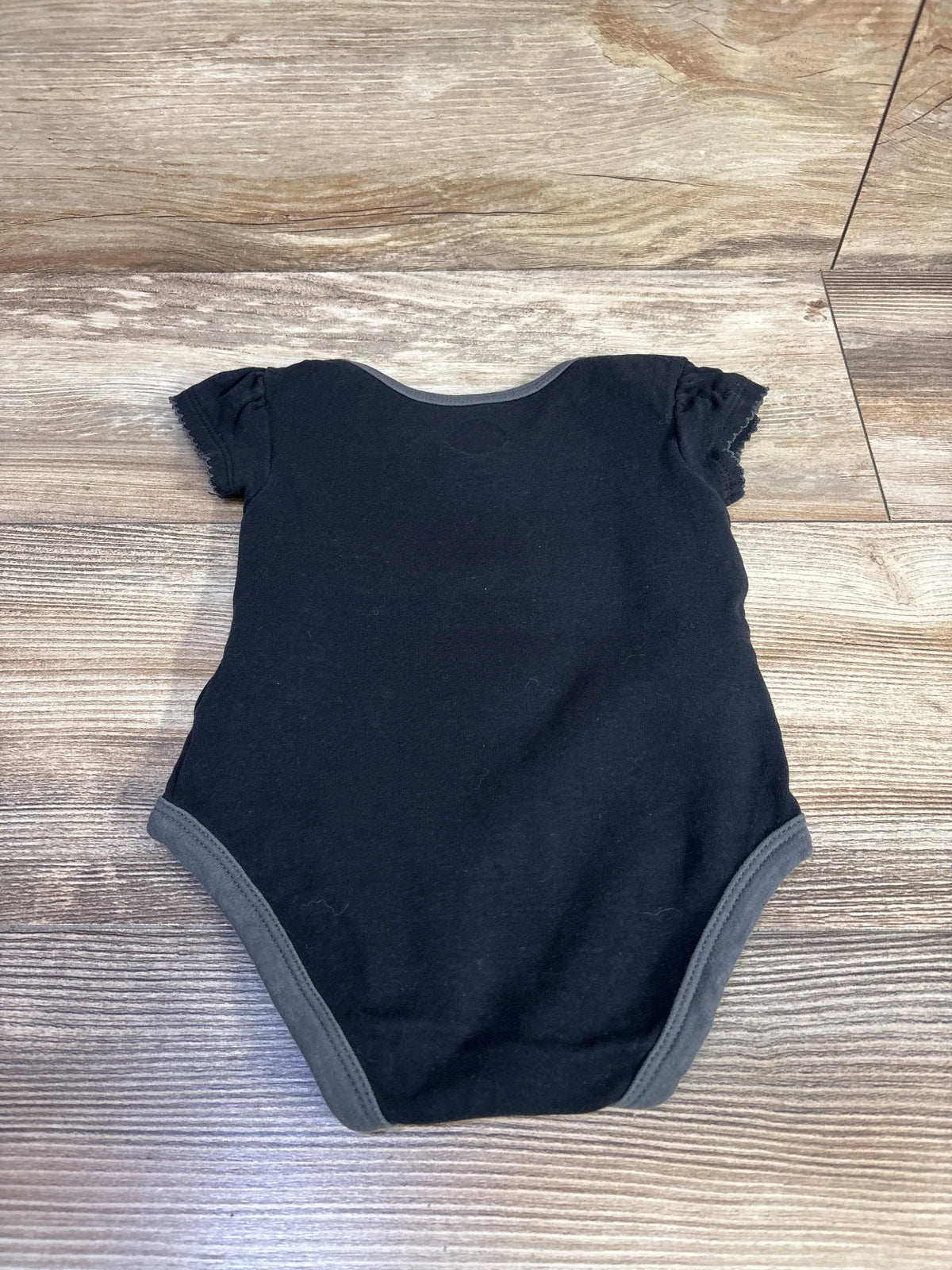 Front view of NHL My First Golden Knights bodysuit in black, size 12 months, with gray trim on wood floor