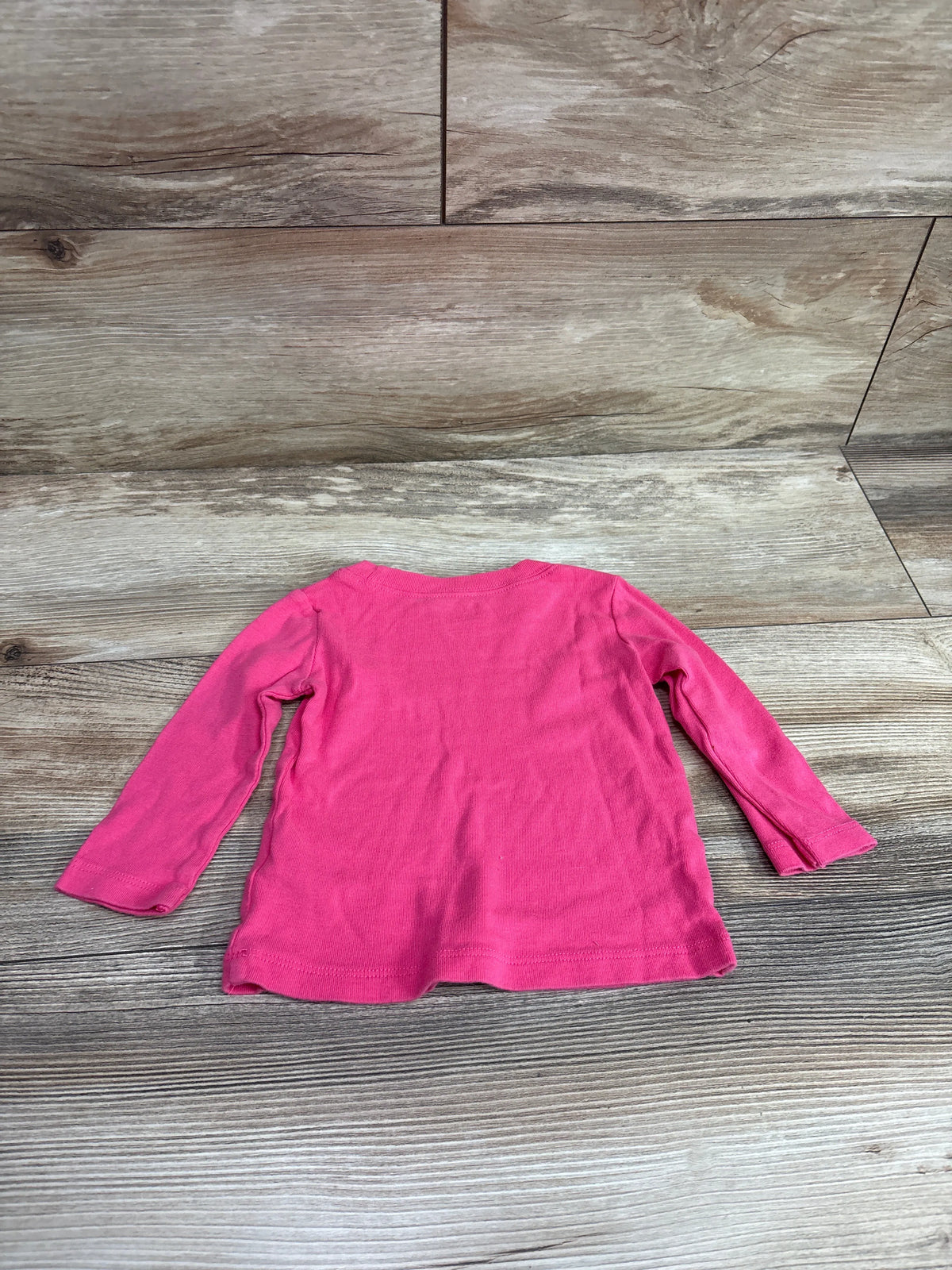 Bright pink Carter's long sleeve baby shirt for size 6-9m on a wooden background