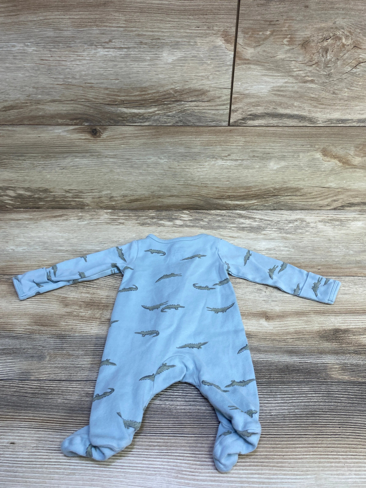 Top view of a blue Simple Joys newborn sleeper showcasing long sleeves, footed legs, and alligator print on a wood floor
