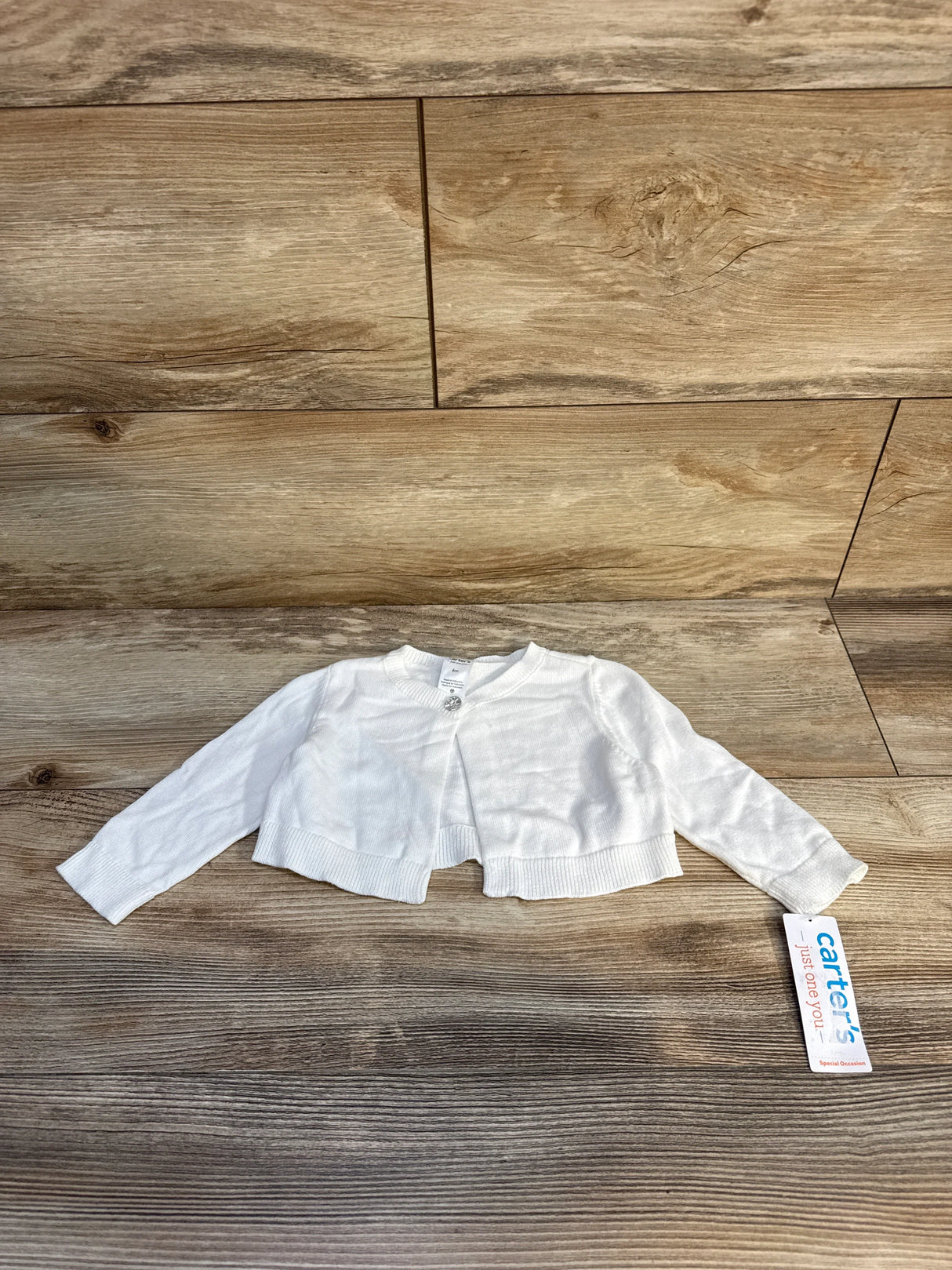 White Carter's baby cardigan with button front on wood background, special occasion tag