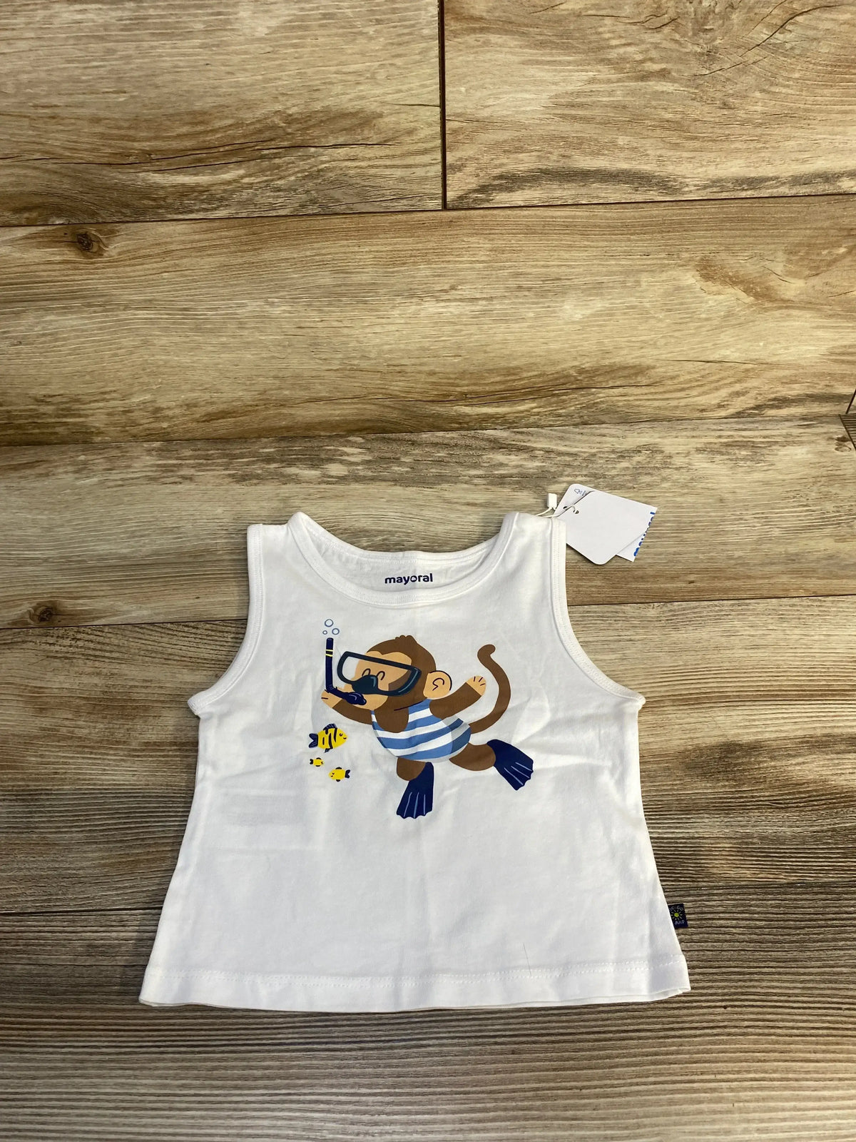 White toddler tank top with snorkeling monkey and fish graphic, laid on wood background