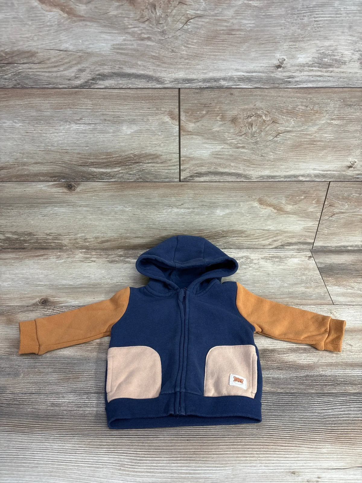 Navy blue and tan toddler hoodie with front pockets, laid flat on wooden floor