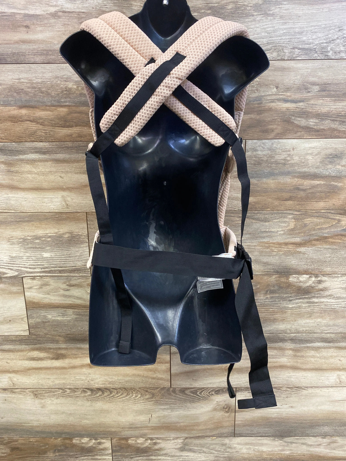 Front view of Momcozy PureHug Air Mesh baby carrier with crossed padded beige mesh straps and black waist belt on wood floor