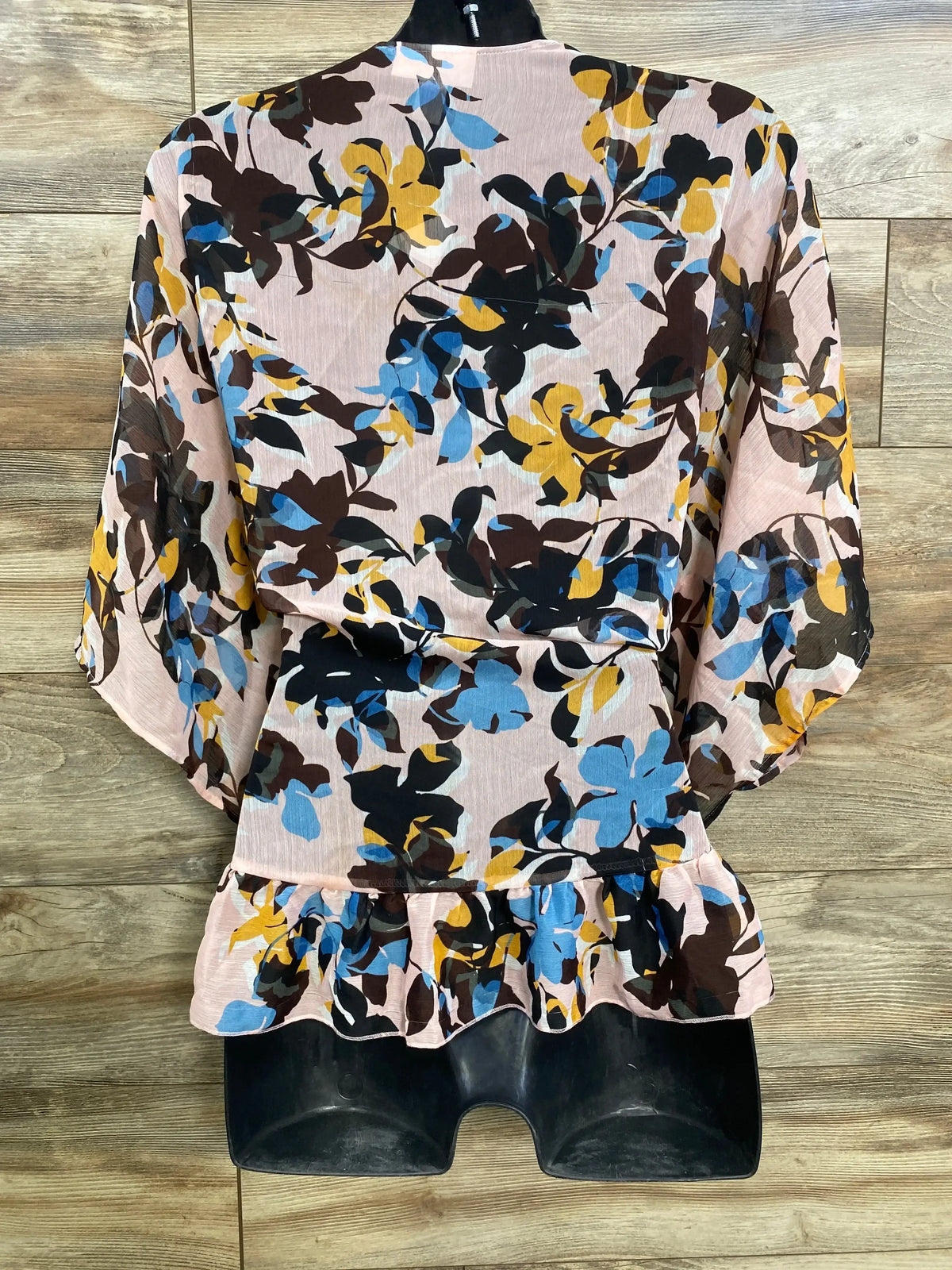 Front view of a pink floral open-front kimono on a black mannequin against a wood-grain background