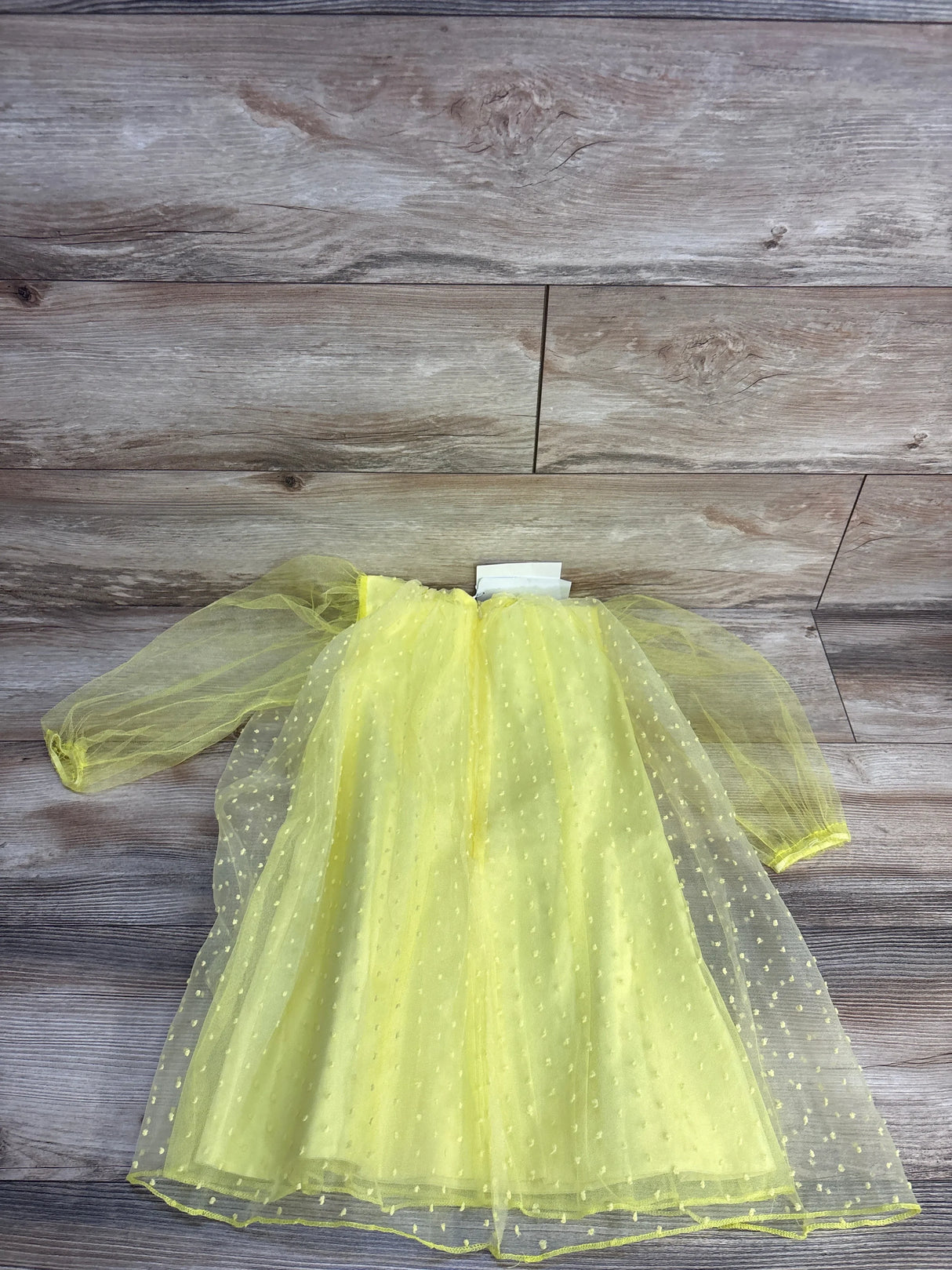 Yellow tulle dress with polka dots for kids, laid on wooden floor