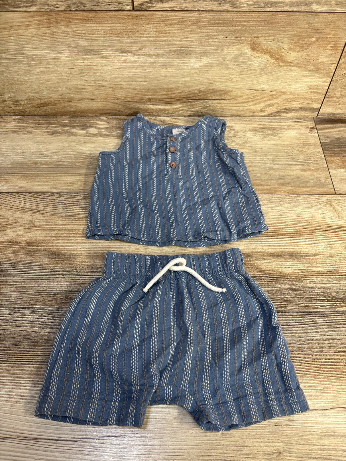 Flat lay of blue 2-piece baby henley tank top and shorts with wooden buttons and white drawstring on light wood background