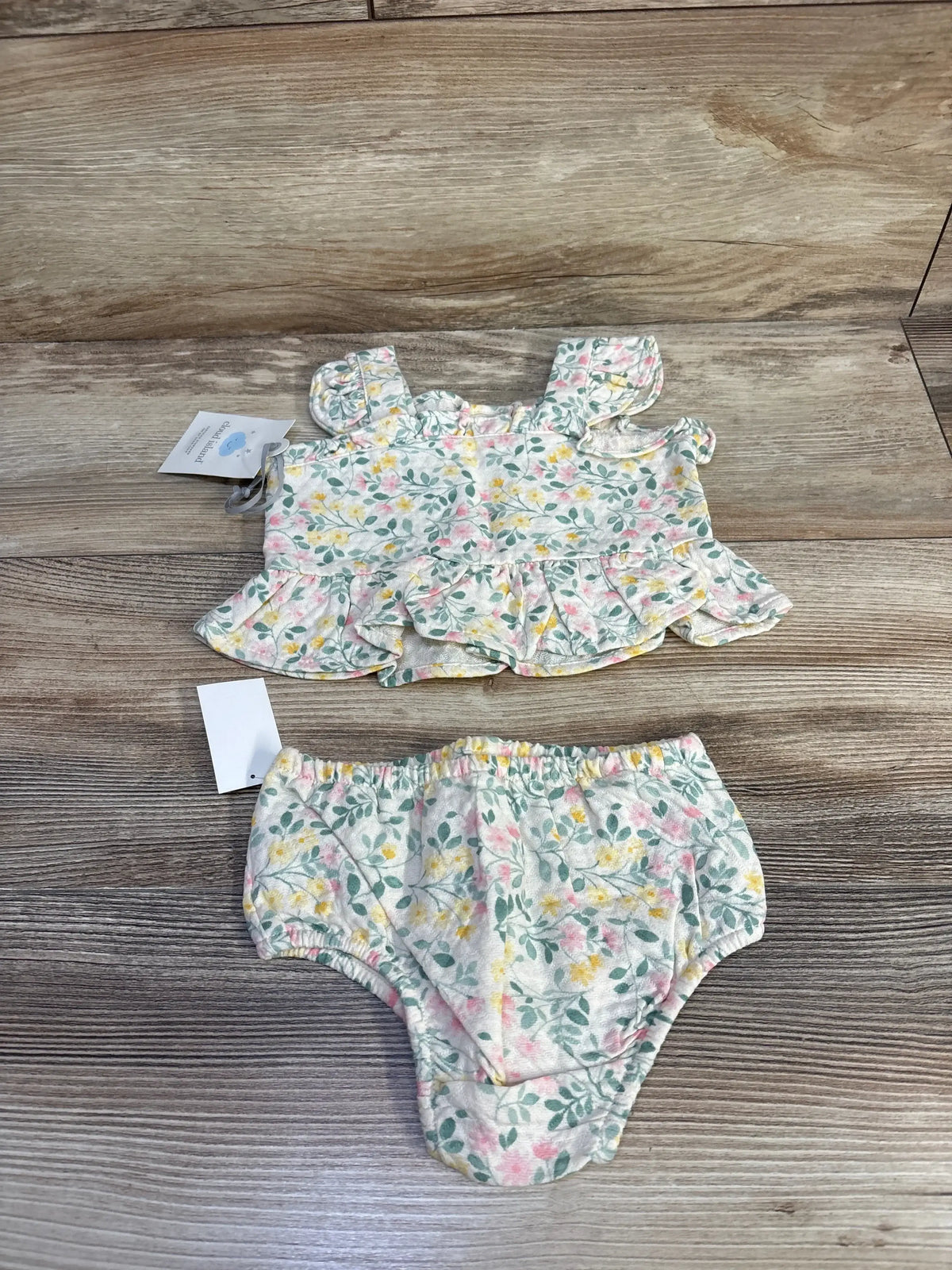 Flat lay of ivory floral baby peplum top with ruffle sleeves and matching bloomers on wood background