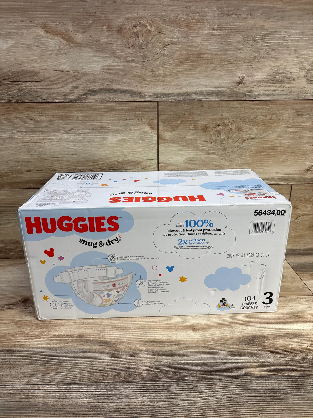 Front view of Huggies Snug & Dry diaper box showing Size 3, 104 diapers, and Leak Lock blowout blocker on a wood surface