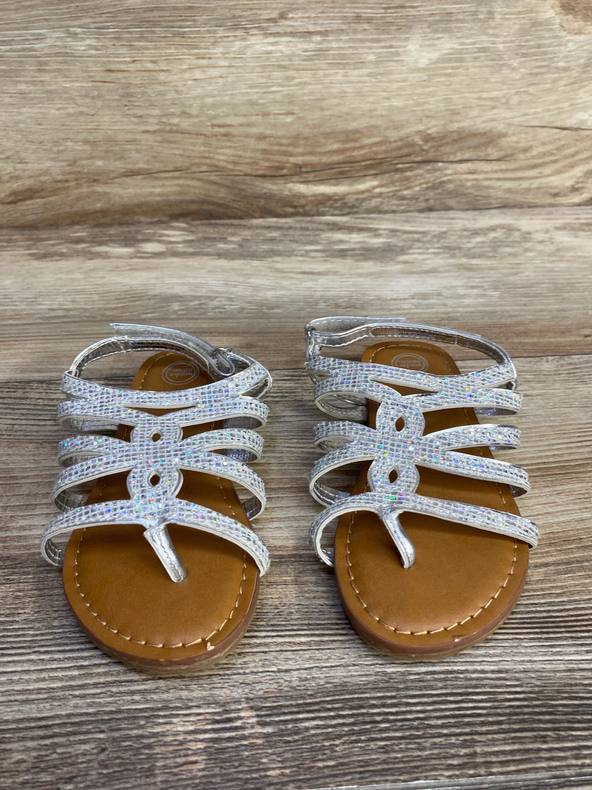 Sparkly silver strappy sandals on wood background, kids summer footwear