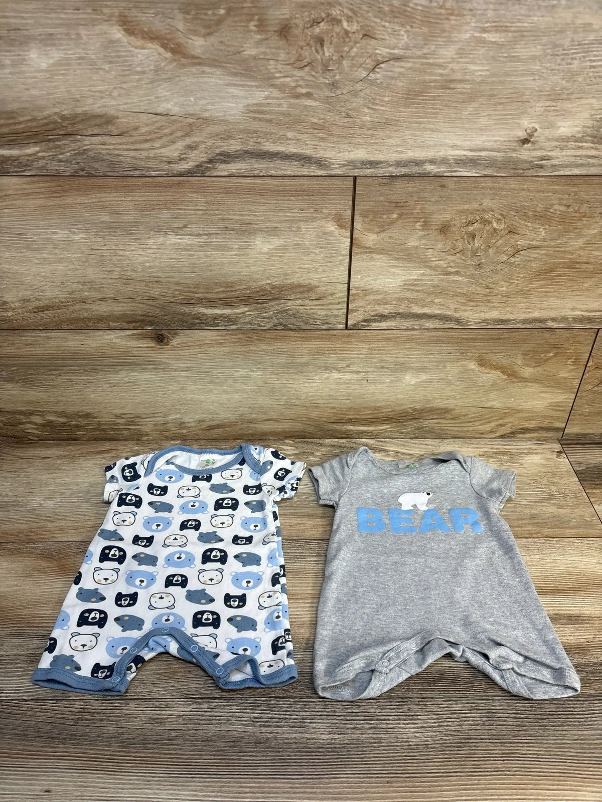 Baby onesies with bear prints and 'BEAR' text on wooden floor