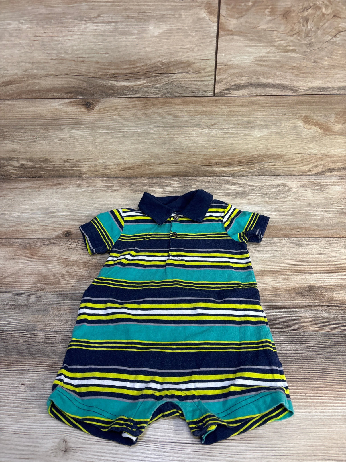 Front flat lay of Simple Joys striped polo shortie romper showing navy, teal, and yellow horizontal stripes, navy collar, and snap crotch on wood background