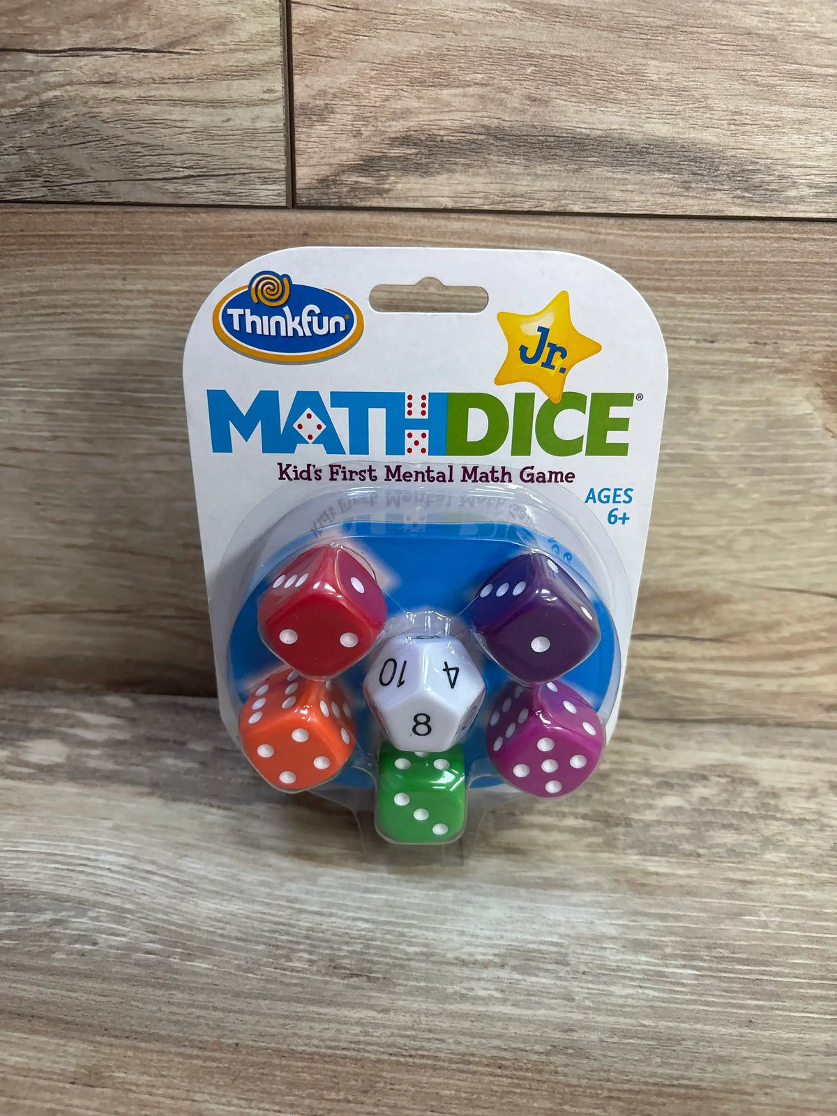 Front view of ThinkFun Jr Math Dice game showcasing six dice in blister packaging on a wood background