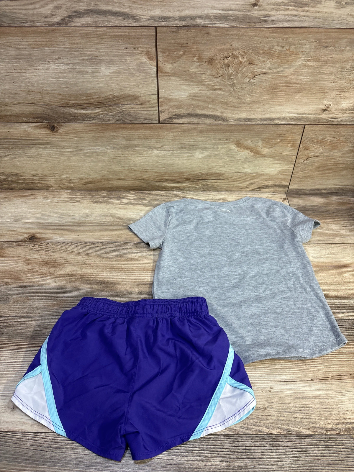 Flat lay of Under Armour two piece shirt and shorts set showing a gray shirt and navy shorts with light blue and white panels on wood flooring