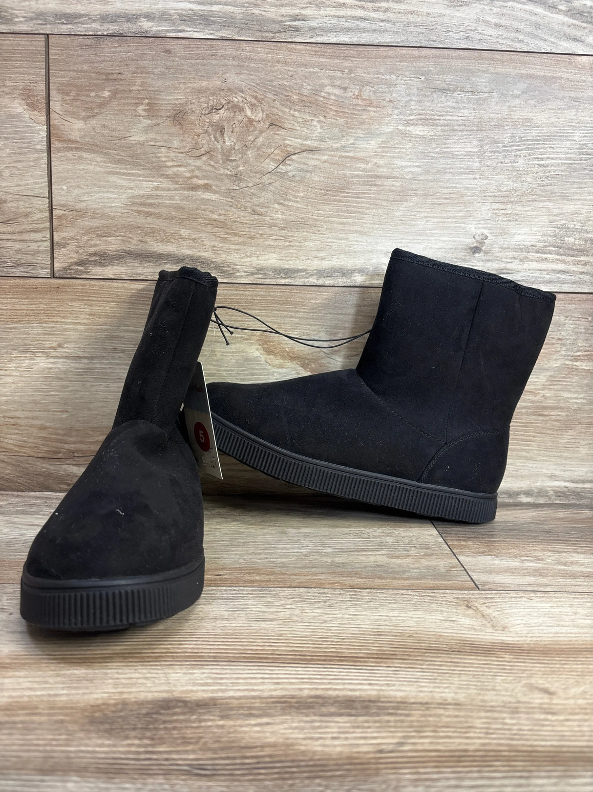 Pair of children's black suede ankle boots with flat rubber soles on wooden floor