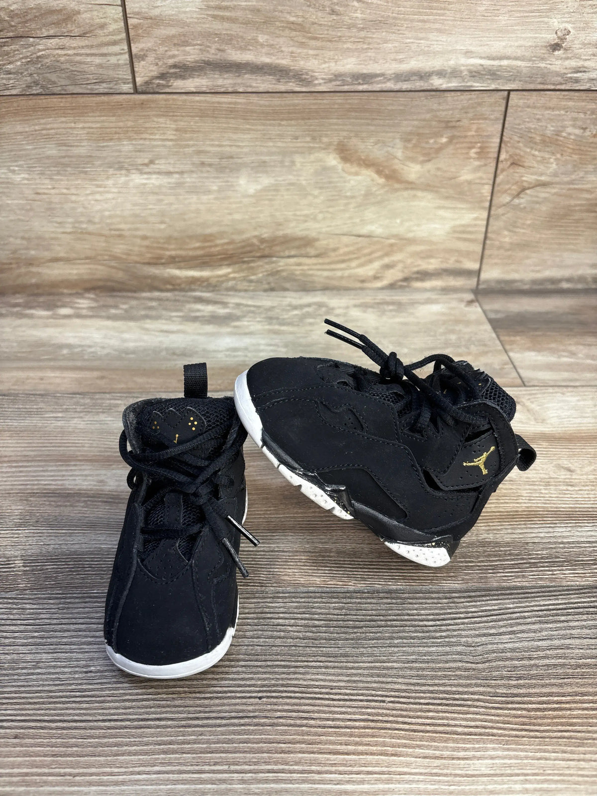 Front and side view of Air Jordan True Flight BT ‘Black’ sneakers showcasing black uppers, gold Jumpman logos, and white outsoles