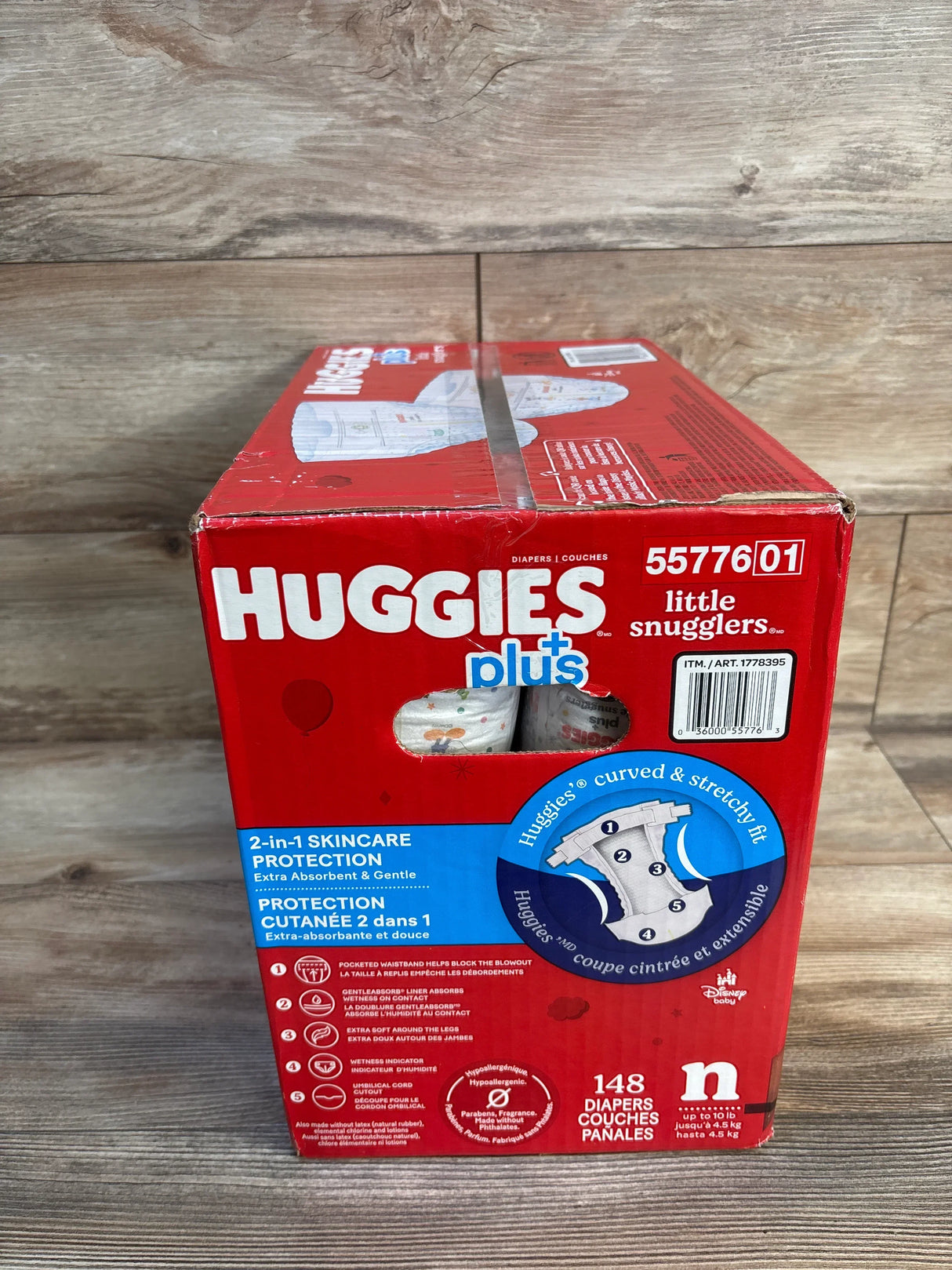 Front view of Huggies Little Snugglers newborn diaper box with 2-in-1 skincare protection, stretchy-fit diagram, on wood floor