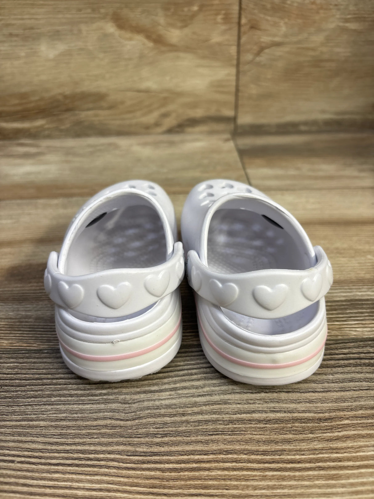 Rear view of Koala Kids white clogs showcasing heart-shaped heel strap and pink-trimmed soles on wooden surface