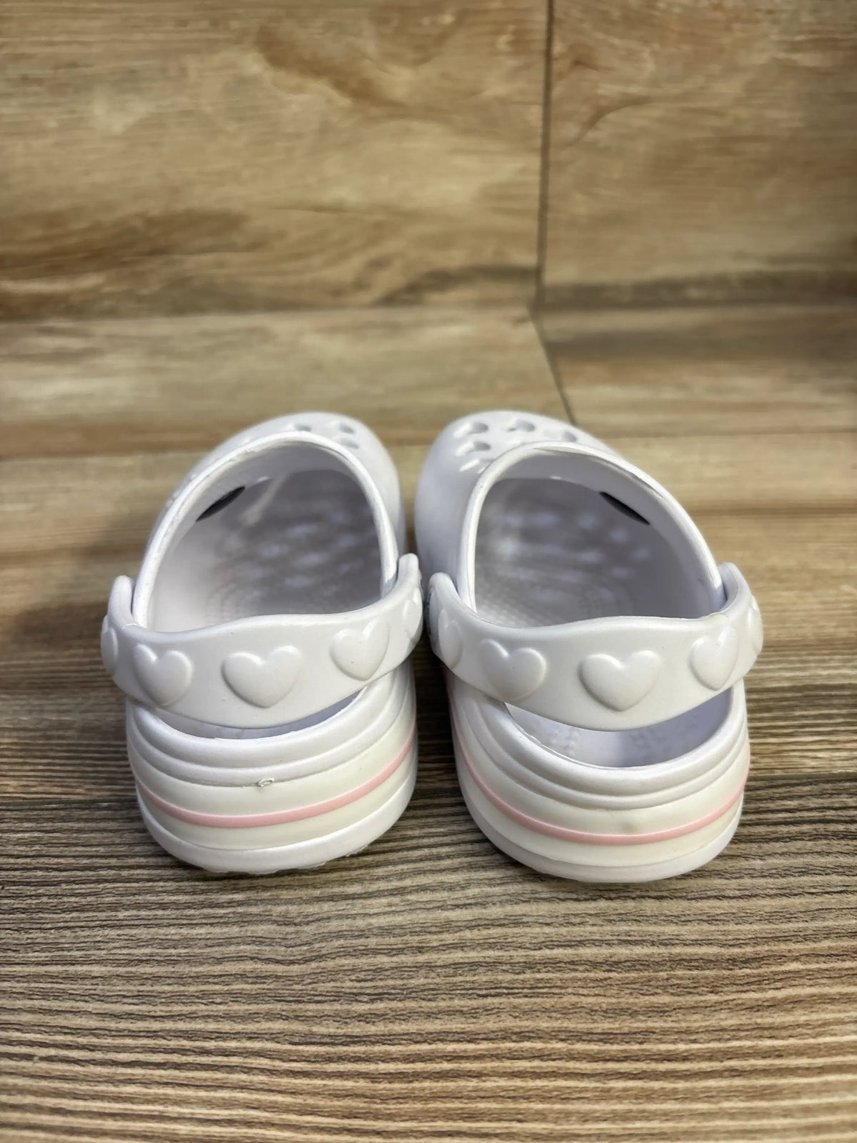 Rear view of Koala Kids white clogs showcasing heart-shaped heel strap and pink-trimmed soles on wooden surface