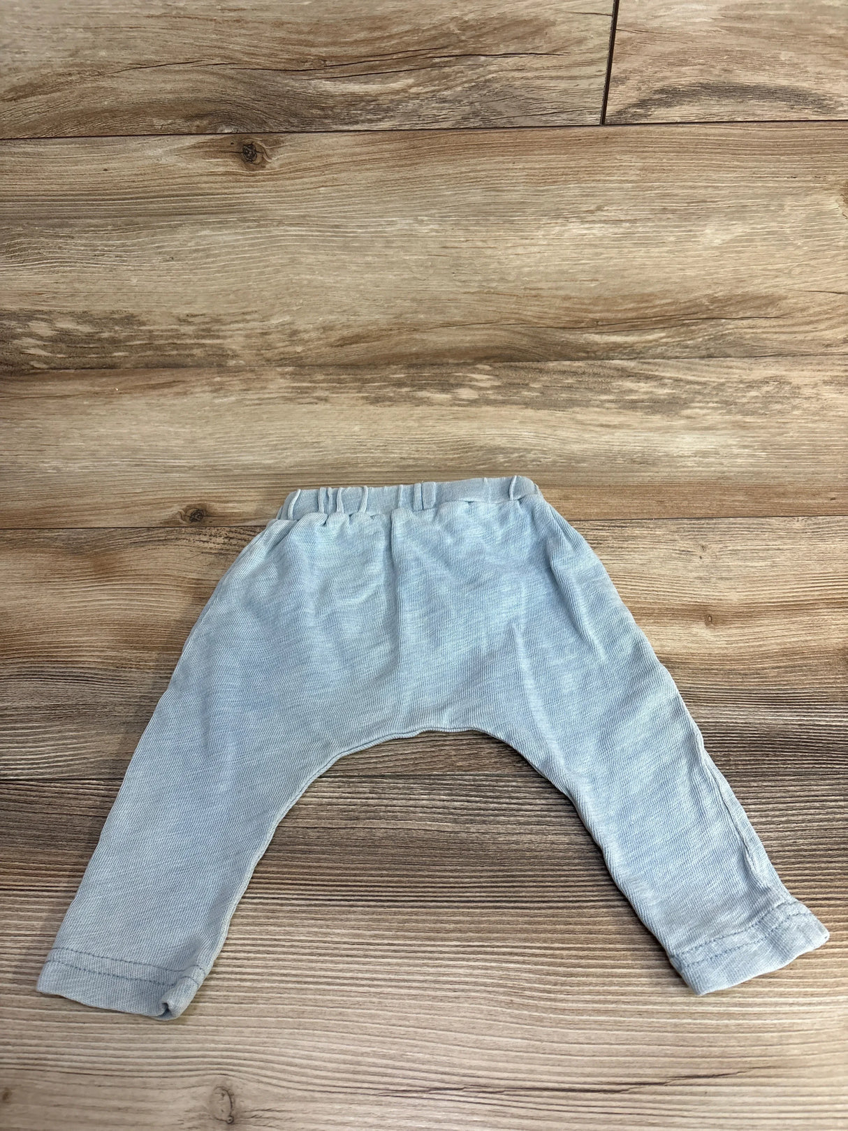 Light gray baby pants with elastic waistband laid flat on wooden surface, children's clothing