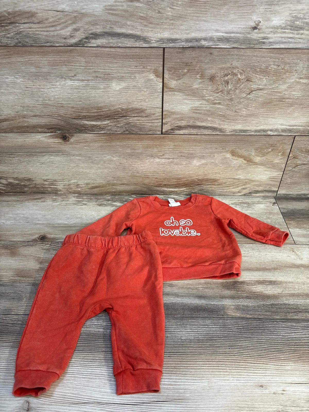 Flat lay of Cat & Jack 2-piece orange toddler sweatshirt and pants set showcasing front oh so lovable text on wood floor