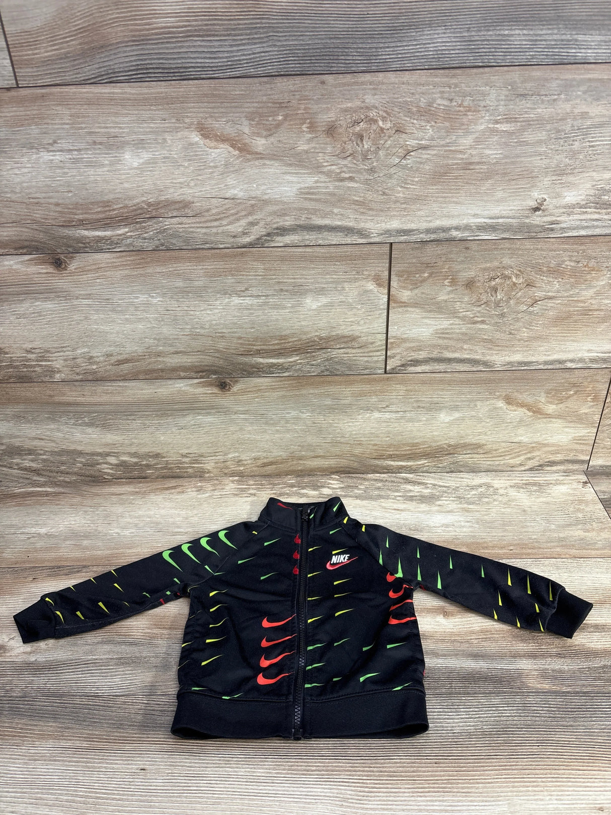 Black Nike toddler jacket with colorful green and red swoosh patterns on wooden floor