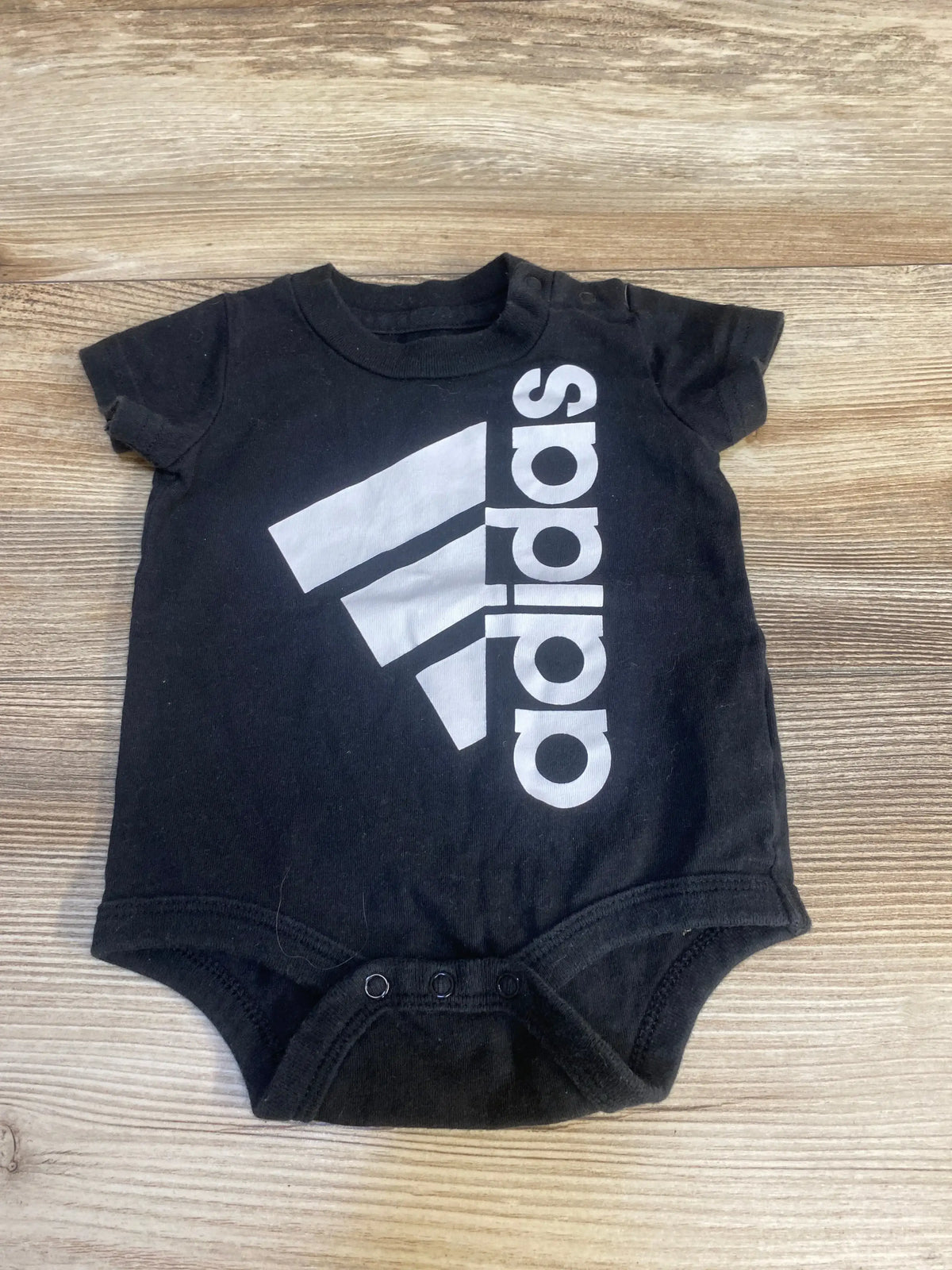 Black short sleeve baby bodysuit with white logo graphic on wooden background