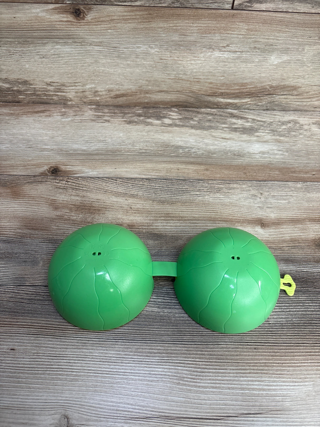 Green plastic connected domes toy with embossed wave patterns on wooden floor