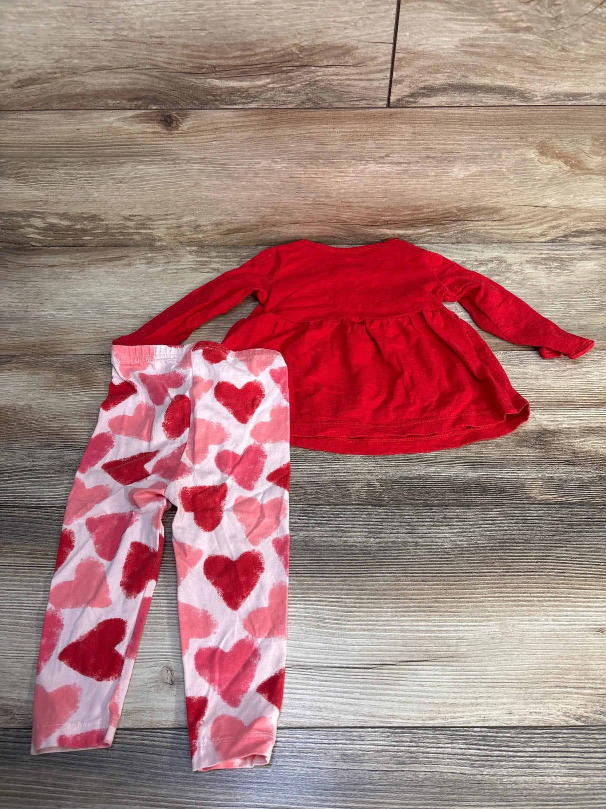 Red long sleeve toddler top with pink heart print leggings on wood background