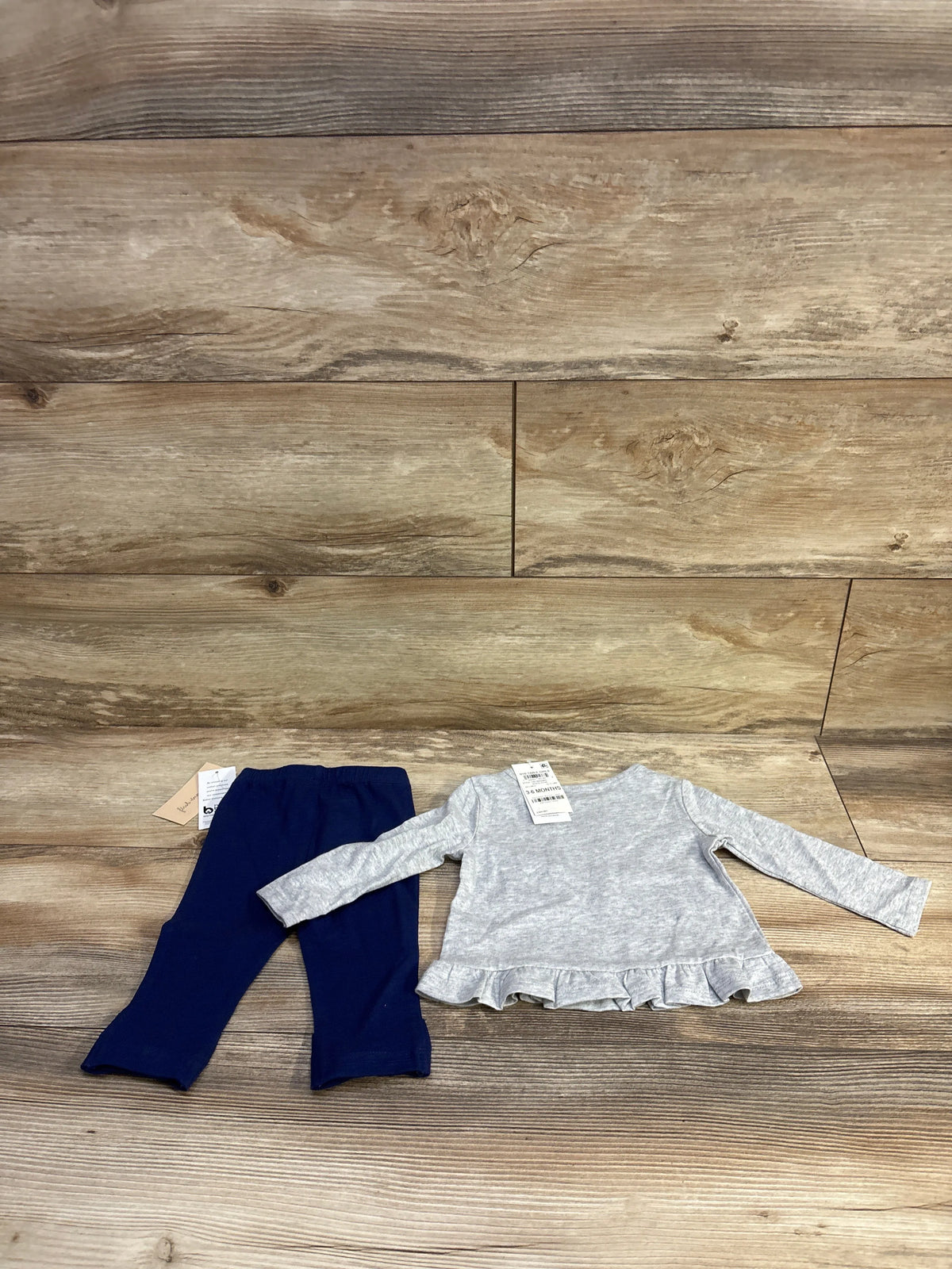 Flat lay of baby two piece set size 3-6 months showing gray long-sleeve peplum top with ruffled hem and navy elastic-waist leggings on wood background