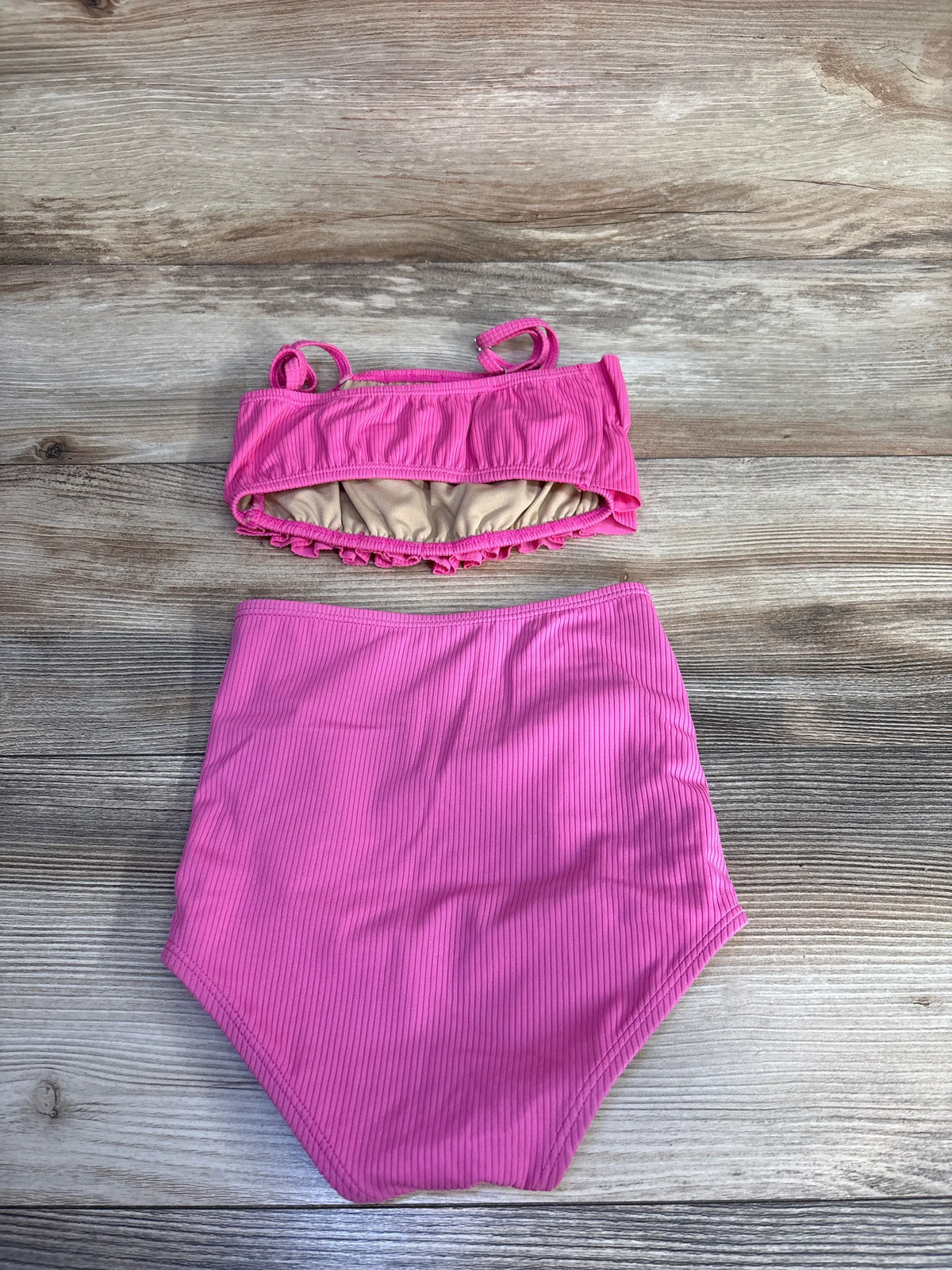 Top down view of a pink two piece ribbed ruffle bikini set showcasing high waisted bottoms and ruffle trim on a wood grain background