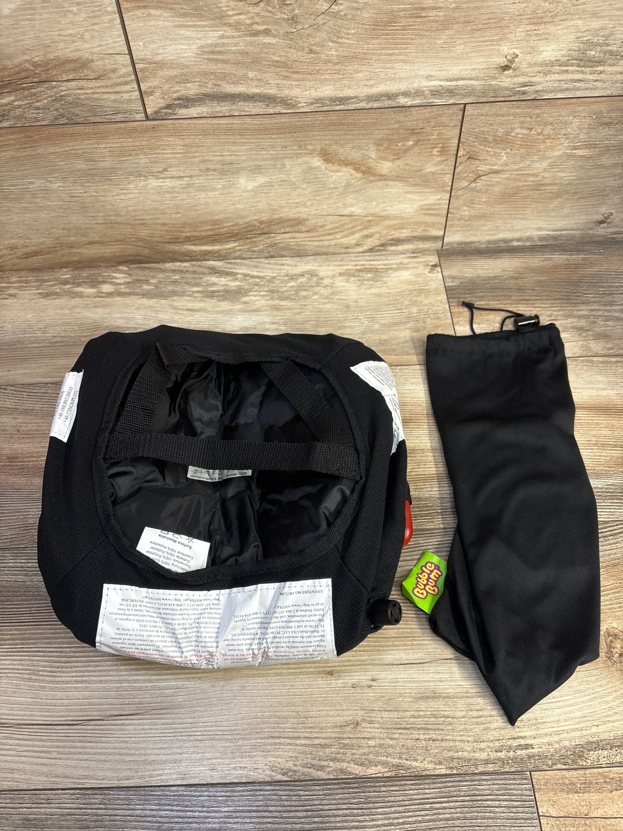 Top down view of Bubble Bum inflatable booster seat in black showcasing included hand pump, black drawstring carry pouch, and green BubbleBum tag on wood floor