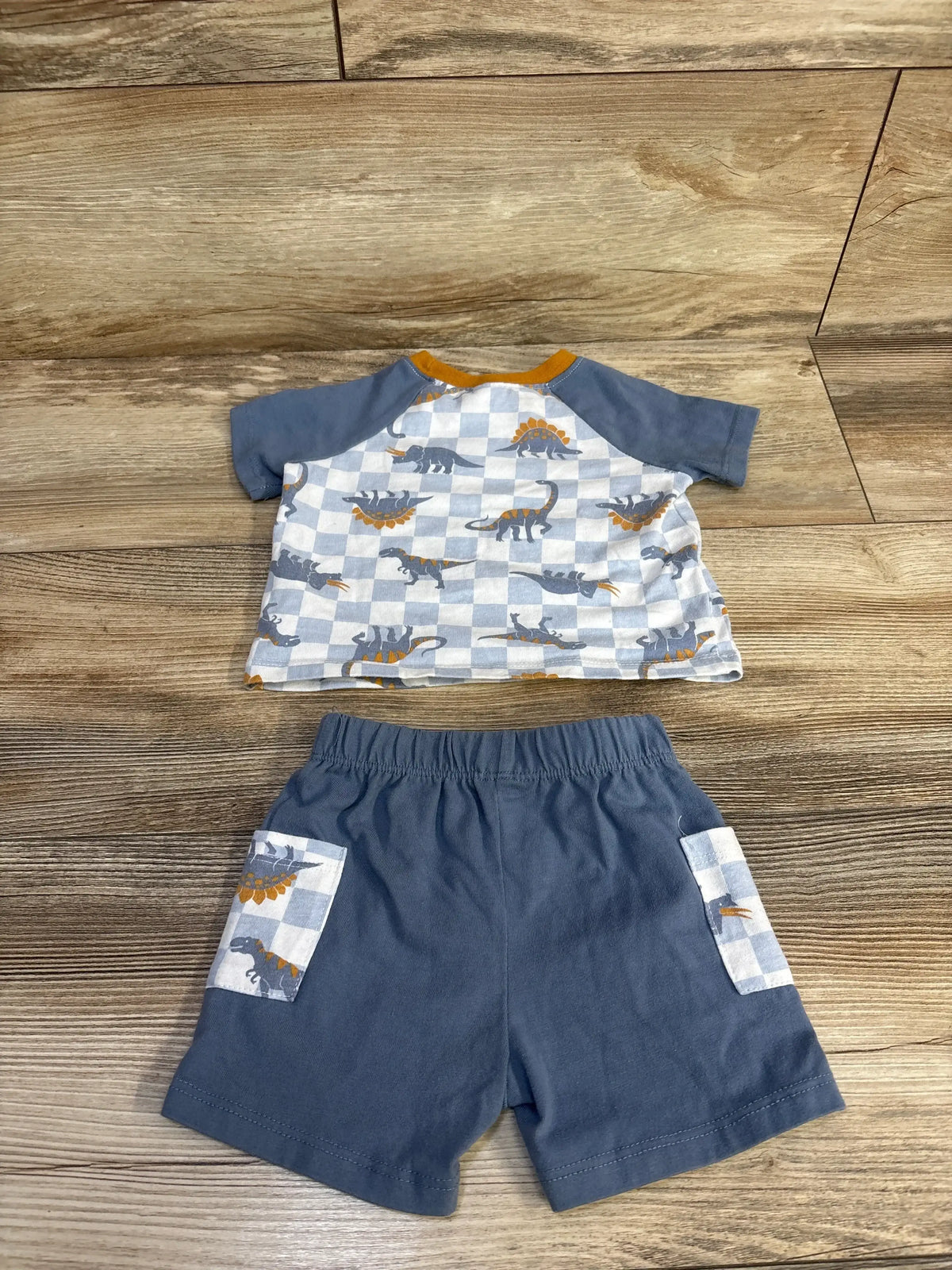 Flat lay of blue baby dinosaur shirt and shorts set with checkered dinosaur print top and solid blue shorts on wood