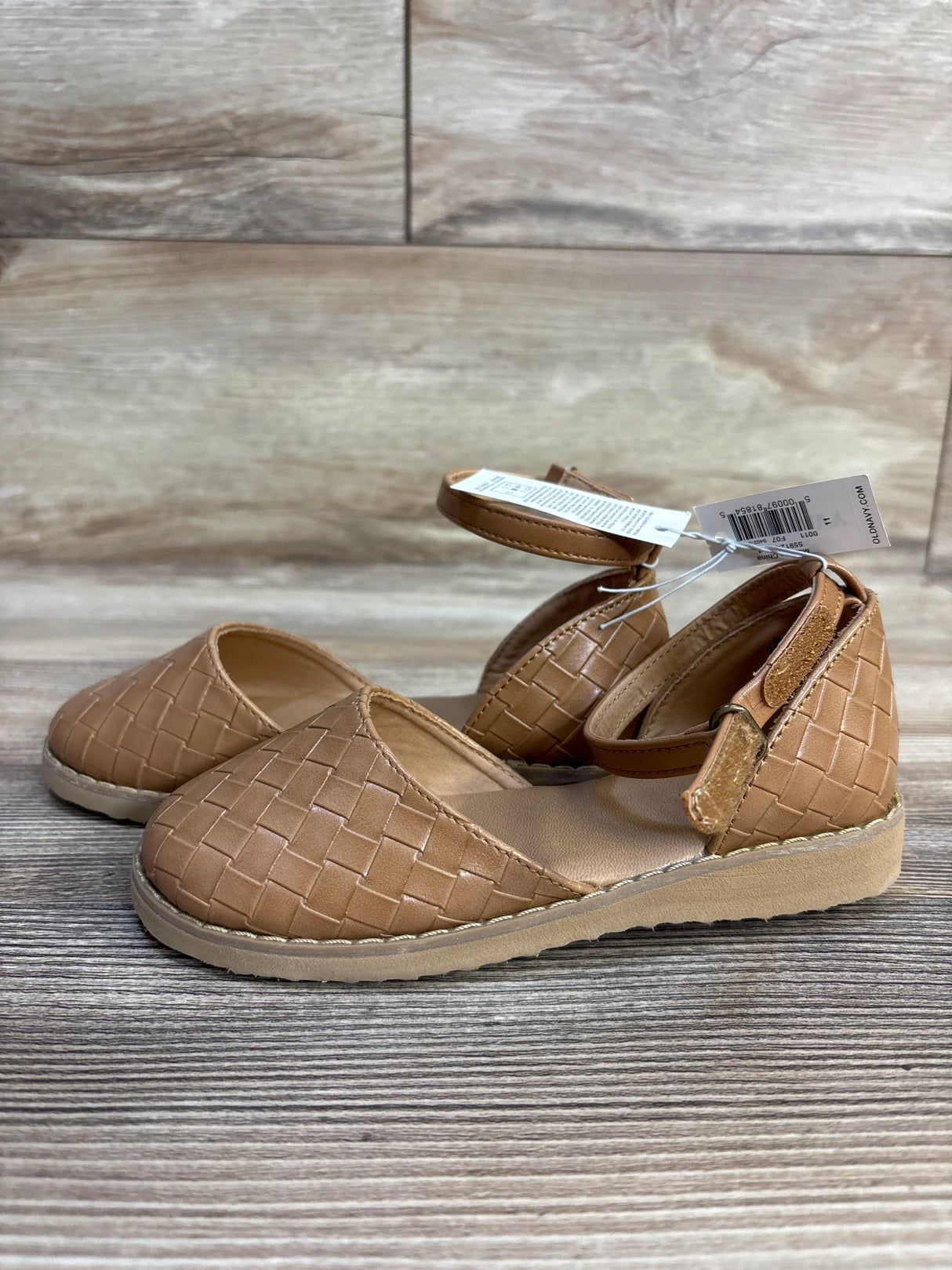 Tan woven toddler dress shoes with ankle strap, displayed on a wooden surface
