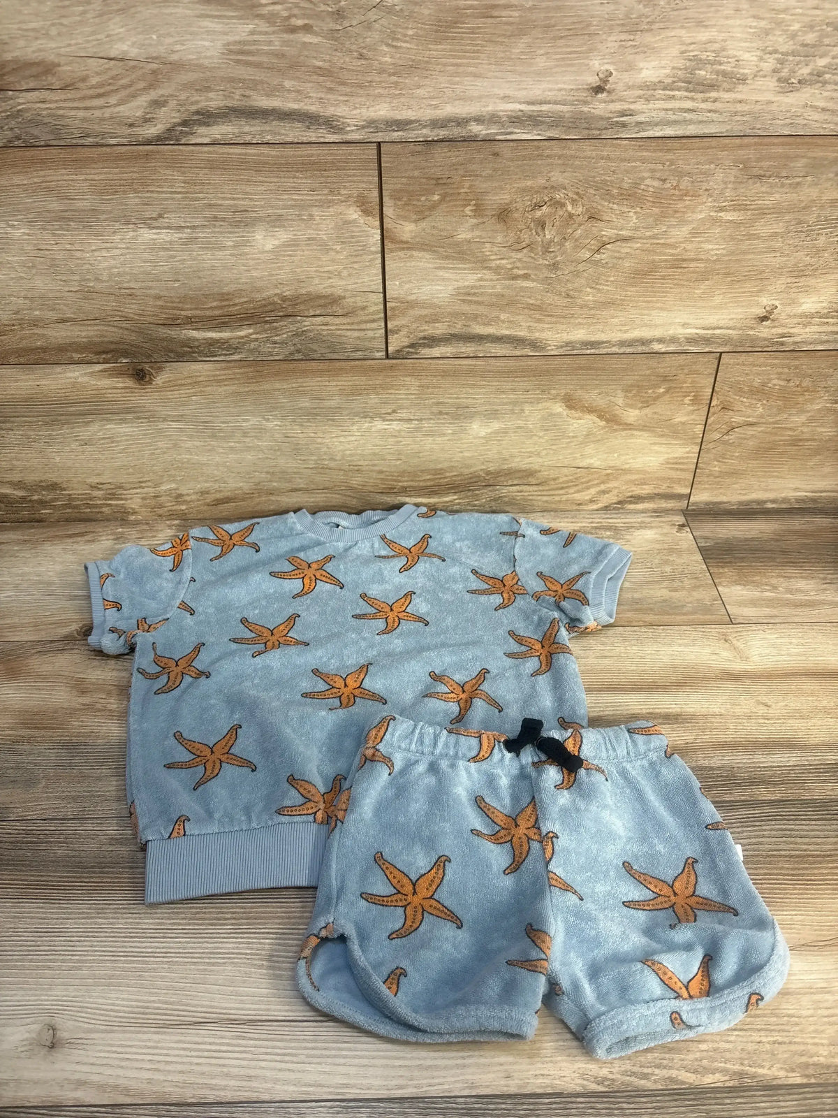 Flat lay of Carlijnq terry cloth 2-piece toddler set (4T), blue short-sleeve top and shorts with orange starfish on wood